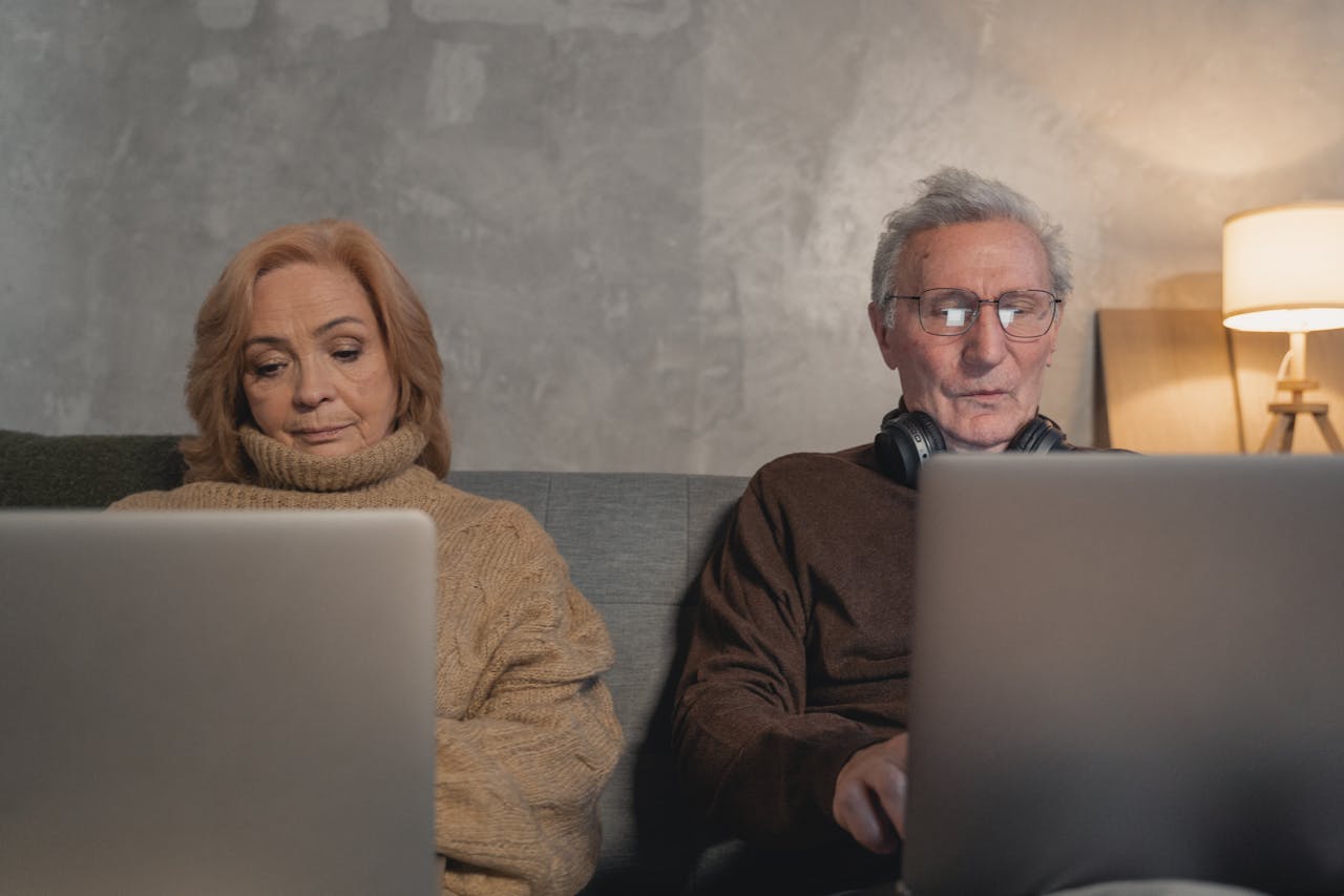 Elderly couple engaging with technology on their laptops at home, showcasing modern senior lifestyle.