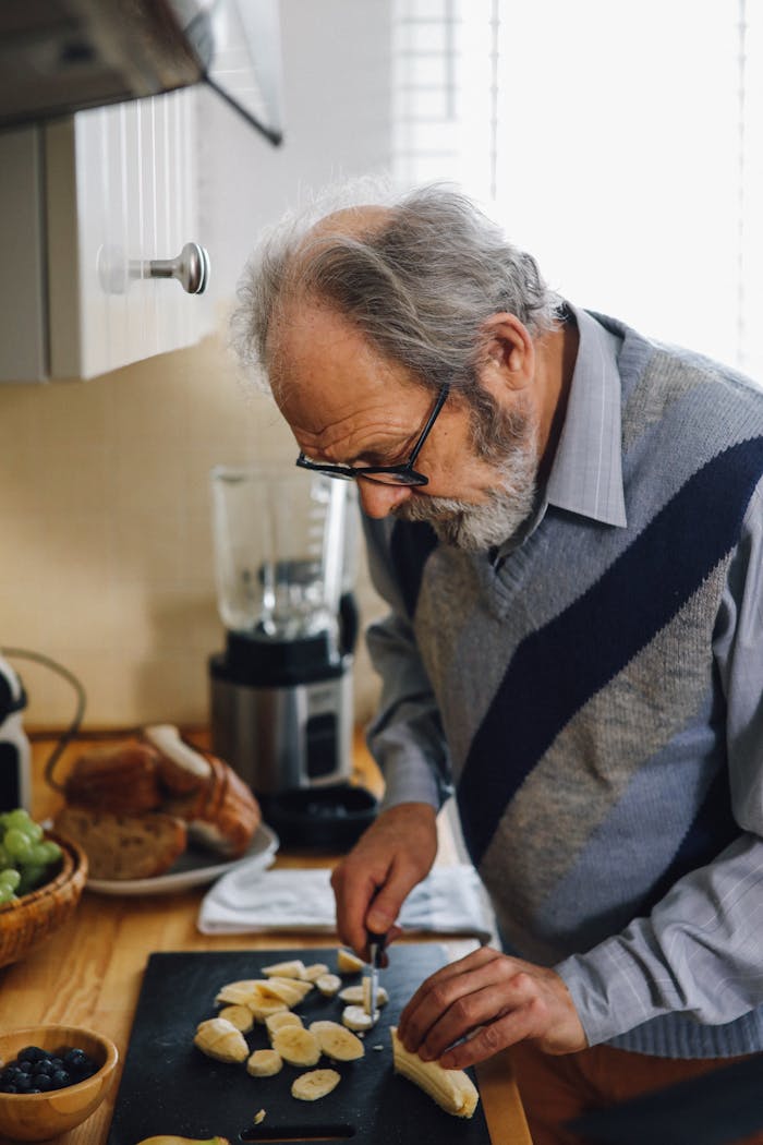 Elderly man preparing fresh bananas on a chopping board in a cozy kitchen setting.